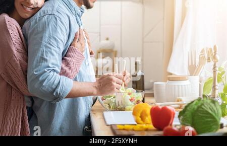 Unkenntlich Mann Kocht Salat In Der Küche, Frau Umarmt Ihn Von Hinten Stockfoto