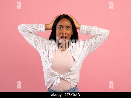 Unglaubliche Nachrichten. Emotionale schwarze Frau hält ihren Kopf in Schock über rosa Studio Hintergrund Stockfoto