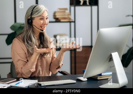 Eine beschäftigte selbstbewusste freundliche schöne reife Asiatin, Geschäftsfrau, Callcenter-Mitarbeiter, Freiberufler, chatten mit Kollegen oder Freunden während eines Videoanrufs, führt Online-Beratung, freundliches Lächeln Stockfoto