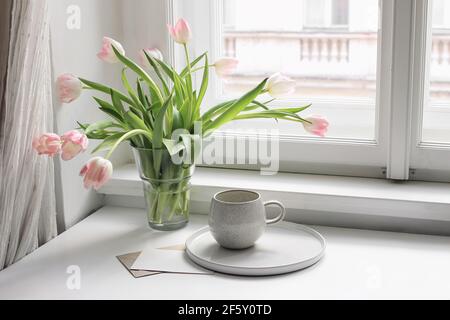 Ostern Frühling Stillleben. tasse Kaffee und Blumenstrauß auf Fensterbank. Rosa Tulpen Blumen in Keramik Vase Topf. Leerer Grußkartenmockup. Zu Hause Stockfoto