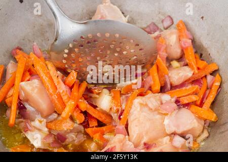 Hühnerstücke werden mit Karotten und roten Zwiebeln darin gebraten Ein Kessel auf dem Grill Stockfoto