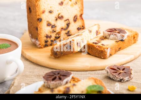 Hausgemachter Kuchen mit Rosinen, getrocknetem Kaki und einer Tasse heißer Schokolade auf grauem Betonboden und Leinentextilien. Seitenansicht, Nahaufnahme, selektiv Stockfoto