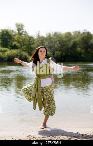 Aktive Mutter macht Yoga am Flussufer mit eingewickelten Rücken Kleines Mädchen Stockfoto