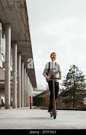 Junger Mann Reiten Elektroroller Fahrzeug vor dem modernen Gebäude Stockfoto