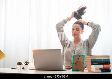 Junge Frau arbeitet mit Computer zu Hause beim Fixieren Haare Stockfoto