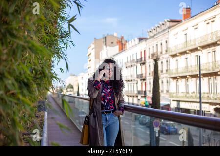 Glückliche afroamerikanische junge Frau im Gespräch mit Handy in der Stadt Stockfoto