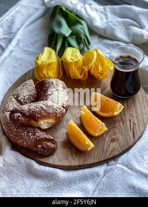 Kaffee mit Brötchen und Orange auf Tulpen Hintergrund Stockfoto