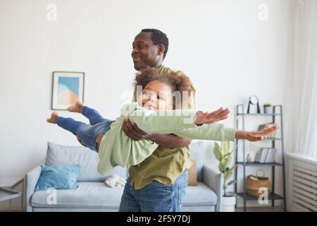 Porträt des verspielten afroamerikanischen Mannes, der mit einer niedlichen Tochter in minimalem Wohnraum spielt Stockfoto