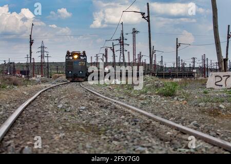 Rudny/Kasachstan - Mai 14 2012: Tagebau von Eisenerz. Eisenbahnzug und Diesellokomotive mit Licht auf Schienen im Steinbruch. Blauer Himmel mit Wolken. Stockfoto