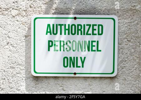 Ein weißes rechteckiges Schild mit grünen Großbuchstaben und einem grünen Rand, der an eine Betonwand gebohrt wurde und besagt, dass nur autorisiertes Personal eintreten darf. Stockfoto