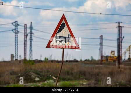 Sokolovo-Sarbay Bergbau-und Verarbeitungsanlage. Handgemachtes Warnschild 'Zug'. Blauer Himmel und verschwommene elektrische Türme und Drähte. Stockfoto