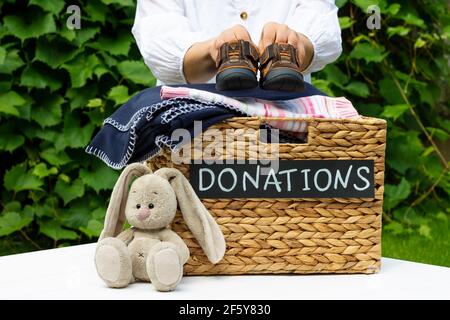 Hände Putting ein Kind Schuhe in eine Box für Spenden auf Grüngrund. Wohltätigkeitskonzept und Spendenkonzept, Kopierraum. Stockfoto