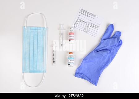 Ausrüstung zur Verabreichung einer Covid19-Impfung mit einer Aufzeichnungskarte. Flach legen mit OP-Maske, Spritzen, Impfstofffläschchen und Handschuh.