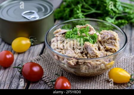 Portion Thunfischsalat mit frischer Petersilie und Kirschtomate auf rustikalem Holztisch. Selektiver Fokus. Stockfoto