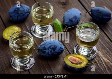 Pflaumenbrand oder Schnaps in Gläsern und frische leckere Pflaumen auf einem Holztisch. Selektiver Fokus. Stockfoto