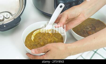 Cremige Linsensuppe in Multi-Herd aus der Nähe in einer Schüssel gekocht, Frau Hände, weißer Hintergrund Stockfoto