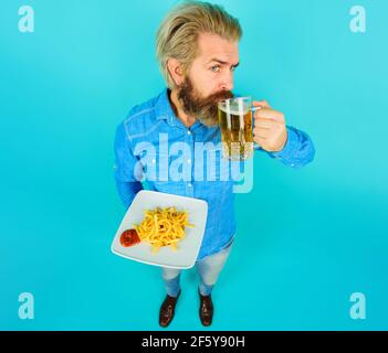 Mann mit Pommes Frites, Ketchup und ein Glas Bier. Bärtiger Kerl mit Pommes Frites. Fast Food, ungesunde Ernährung, Junk-Food. Stockfoto