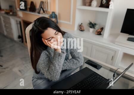 Gestresste junge Frau mit Brille und Pullover sitzt Im Wohnzimmer zu Hause ist es leid zu studieren Im Online-Unterricht Stockfoto