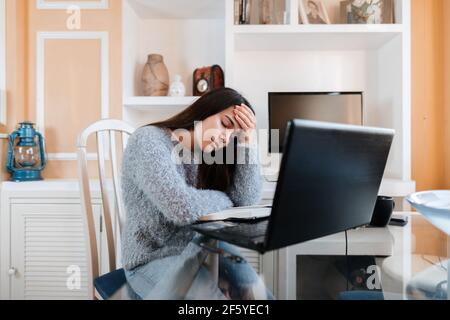 Gestresste junge Frau mit Brille und Pullover sitzt Im Wohnzimmer zu Hause ist es leid zu studieren Im Online-Unterricht Stockfoto