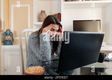 Gestresste junge Frau mit Brille und Pullover sitzt Im Wohnzimmer zu Hause ist es leid zu studieren Im Online-Unterricht Stockfoto