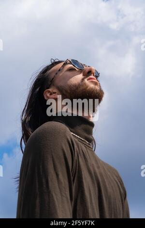 Porträt eines Mannes mit Sonnenbrille, Augen geschlossen, inspiriert. Denken. Junger Mann mit langen Haaren und Bart. Stockfoto