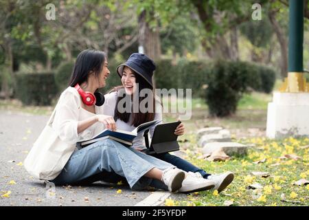 Zwei glückliche Studenten sitzen und unterhalten sich auf einem Campus im Park. Stockfoto