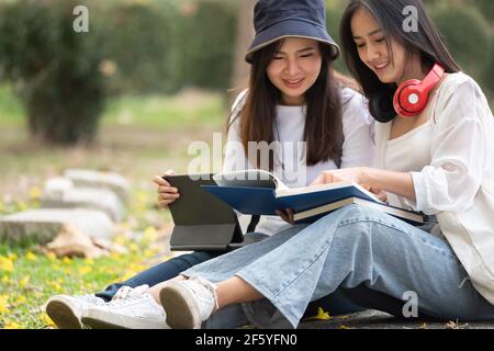 Zwei glückliche Studenten sitzen und unterhalten sich auf einem Campus im Park. Stockfoto