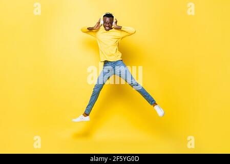 Glücklicher junger afrikanischer Mann mit Kopfhörern Musik hören und Springen in gelb isoliert Studio Hintergrund Stockfoto