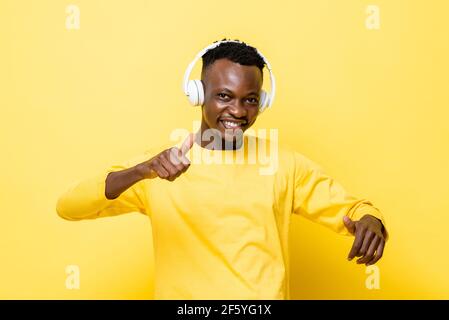 Glücklich lächelnder junger afrikanischer Mann in lässiger Kleidung genießt das Zuhören Zu Musik mit Kopfhörern und Tanz über gelbe Studiowand Hintergrund Stockfoto