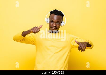 Glücklich lächelnder junger afrikanischer Mann in lässiger Kleidung genießt das Zuhören Zu Musik mit Kopfhörern und Tanz über gelbe Studiowand Hintergrund Stockfoto