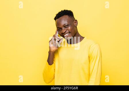 Lächelnder junger afrikanischer Mann, der auf dem Handy in Gelb spricht Isolierter Studiohintergrund Stockfoto