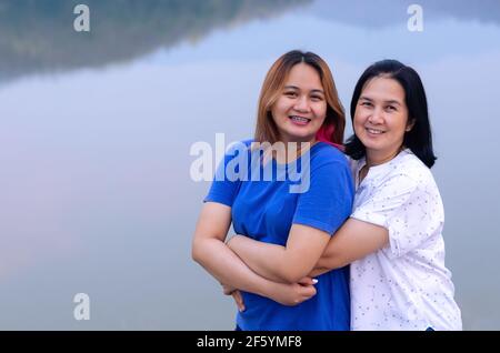Alleinerziehende asiatische Mutter und ihre Teenager Tochter umarmen sich zusammen auf See Hintergrund mit Schatten des Berges. Muttertagskonzept Stockfoto