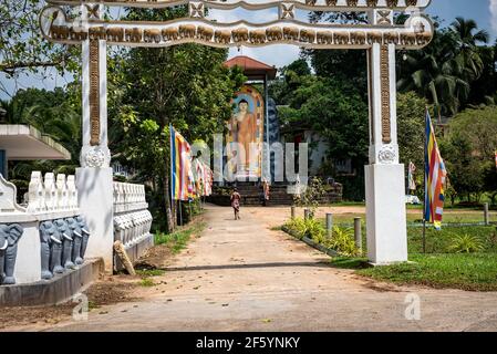 Eingang zu einem buddhistischen Tempel mit einem Mann heruntergelaufen Eine Gasse in einem Lendenschurz vor einem großen Bild des Buddha auf der Insel Sri Lanka Stockfoto