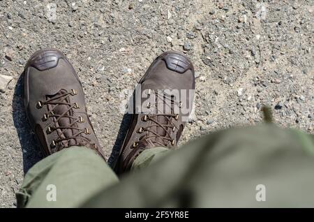 Beine in braunen Militärstiefeln und grünen Hosen. Soldat steht in Uniform auf dem Bürgersteig draußen. Blick von oben in einem Winkel. Stockfoto