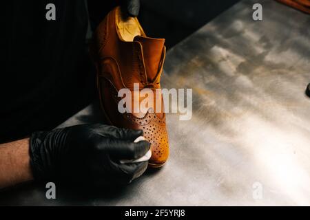 Nahaufnahme Hände des Schusters tragen schwarze Handschuhe reiben Farbe auf Zehenspitze hellbrauner Lederschuhe mit Fingern. Stockfoto