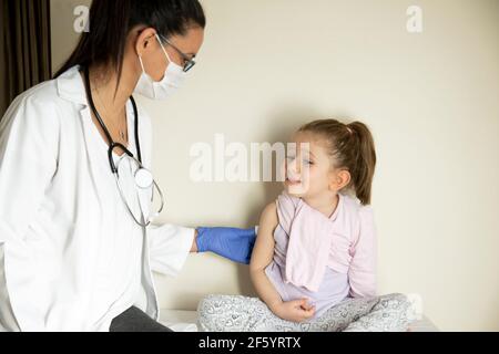 Molliges kleines Mädchen bei der pädiatrischen Untersuchung durch ihren Arzt. Geimpft von ihrem Arzt. Selektiver Fokus. Covid Impfstoff Baby Stockfoto