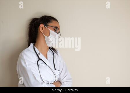 Junge Ärztin macht ein Nickerchen, müde und lehnt an die Wand. Speicherplatz Kopieren. Selektiver Fokus. Stockfoto