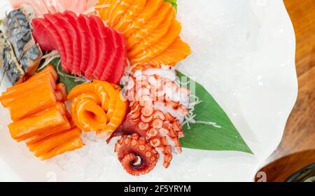 Japanisches Essen Combo Set. Lachs, Thunfisch-Sashimi, Riesenoktopus und Krabbenstäbchen servieren mit zerdrücktem Eis auf weißem Teller auf dem Restauranttisch. Fischfleisch. Stockfoto