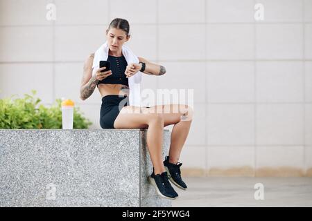 Serious fit Frau Ruhe nach dem Training und Überprüfung ihres Herzens Bewerten und Gesamtaktivität über Anwendungen auf Smartphone und Smartwatch Stockfoto