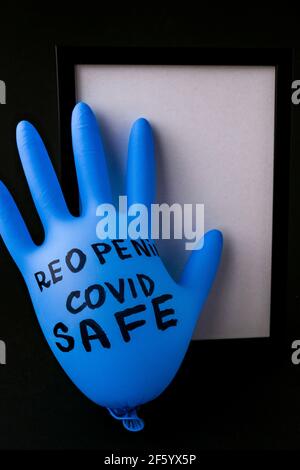 Aufgeblasster blauer Latex-OP-Handschuh auf schwarzem Hintergrund. Covid Safe wieder öffnen. Öffnen Sie den Text, der auf einem medizinischen Handschuh geschrieben ist. Neuer Normalwert Stockfoto