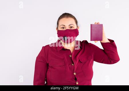 Geschäftsfrau, Reisende in einer medizinischen Schutzmaske auf ihrem Gesicht, zeigt Pass, stehend auf einem grauen Hintergrund. Konzept der Quarantäne in Stockfoto