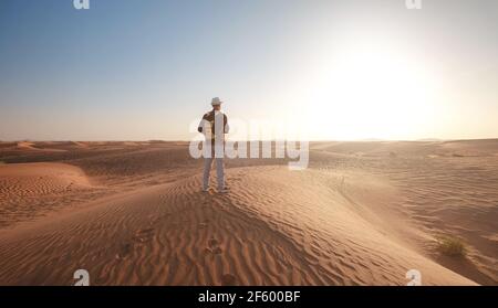 Wüstenabenteuer. Junger Mann mit Rucksack zu Fuß auf Sanddüne. Die Geisterstadt Al-Madam in der Nähe von Dubai, Vereinigte Arabische Emirate. Idee und Konzept von Succe Stockfoto