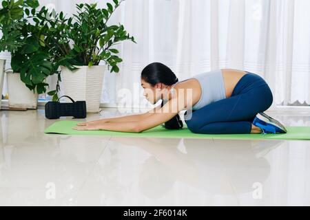 Junge asiatische Frau in Balasana entspannen oder Kinder Pose auf Yogamatte zu Hause nach dem Training Stockfoto