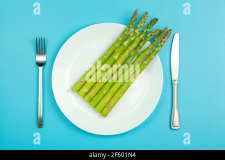 Spargel auf weißem Teller auf blauem Hintergrund. Frischer Gemüsespargel für eine gesunde Ernährung. Gemüse und gesunde Ernährung Konzept. Hochwertige Fotos Stockfoto