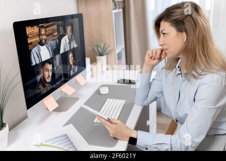 Konzentrierte schöne Geschäftsfrau nutzt Computer, mit einem Video-Meeting. Elegante, stilvolle Frau sitzt am Schreibtisch und diskutiert mit Stockfoto