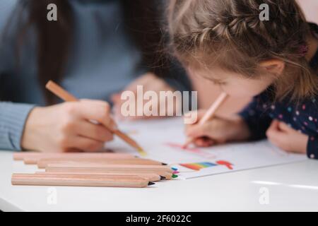 Adirable kleines Mädchen mit ihrer schönen jungen Mutter zeichnet in das Album mit Farbe Pensins. Nettes Mädchen malt Malvorlagen zu Hause während quararntin Stockfoto