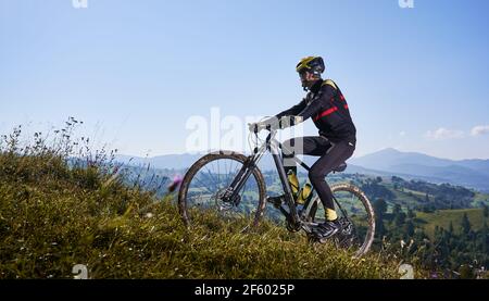 Fröhlicher Radler, der unter blauem Himmel Fahrrad bergauf fährt. Stockfoto