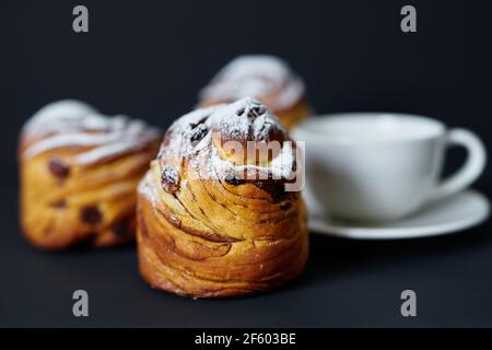 Leckere frisch gebackene Cruffins mit weißer Tasse Kaffee oder Tee auf dunklem Hintergrund. Traditionelles Osterkuchen- oder Bäckerkonzept. Hochwertige Fotos Stockfoto