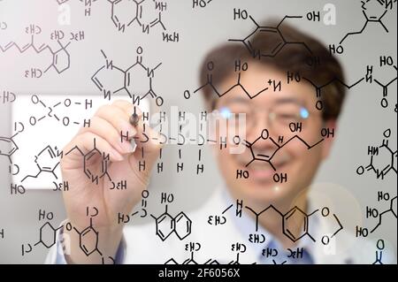 Asiatischer Wissenschaftler mittleren Alters lächelt und schreibt chemische Formeln auf transparentem Glas. Stockfoto