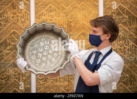 Ein Angestellter in Sothebys Auktionshaus, London, hält ein silberfarbenes Kuschelbecken aus dem zwölften Jahrhundert mit astrologischen Mustern, das im Rahmen des bevorstehenden Verkaufs der Künste der islamischen Welt und Indiens am 31st. März £1.500.000 - £1.000.000 zu erstehen ist. Bilddatum: Montag, 29. März 2021. Stockfoto